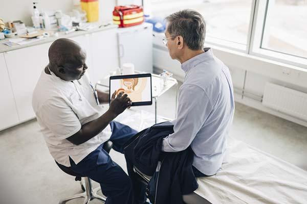 high angle view of a doctor holding a tablet with an illustration of male reproductive organs, showing a male patient during a consultation.